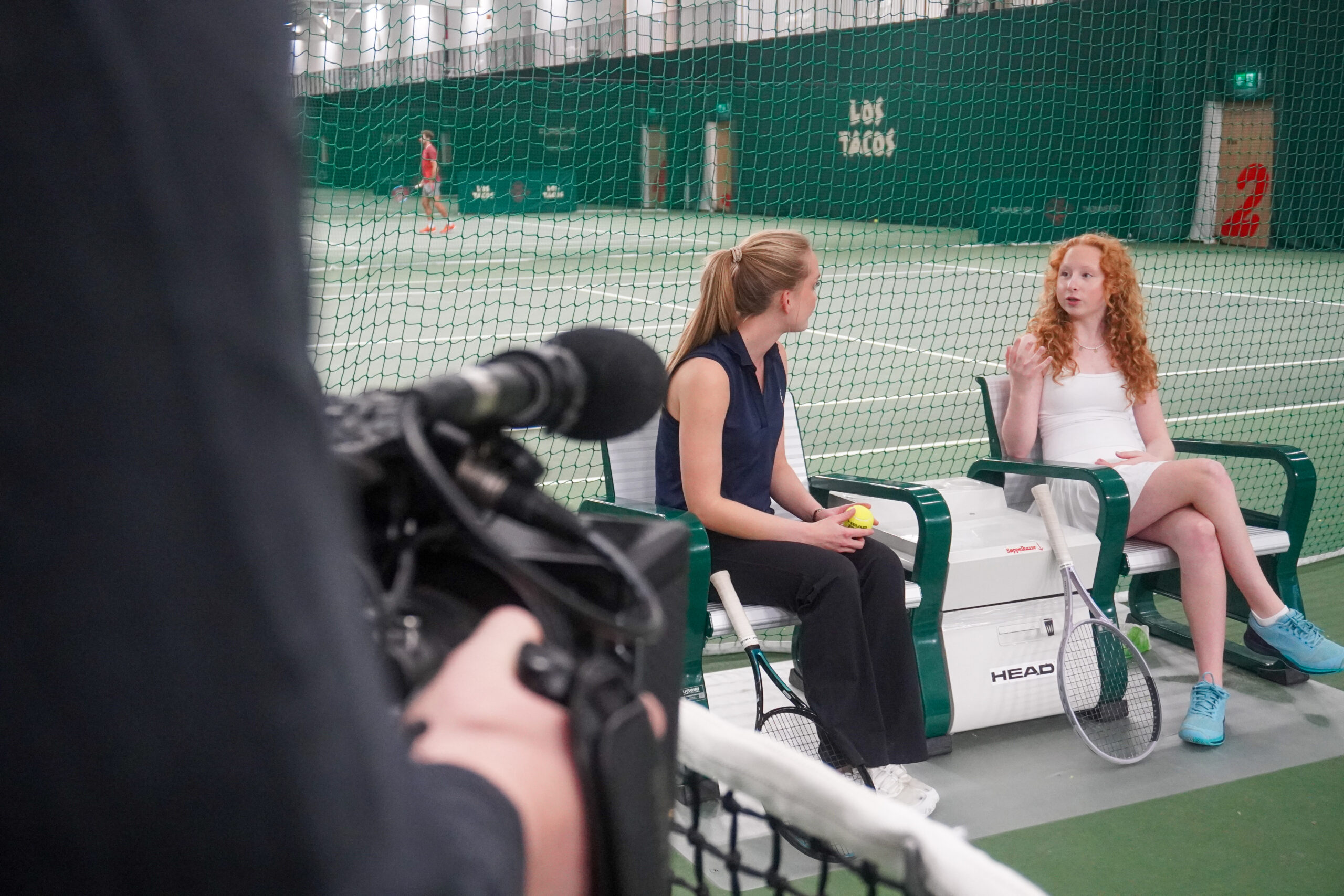 Isabella og treneren hennes i samtale på tennisbanen under innspillingen.